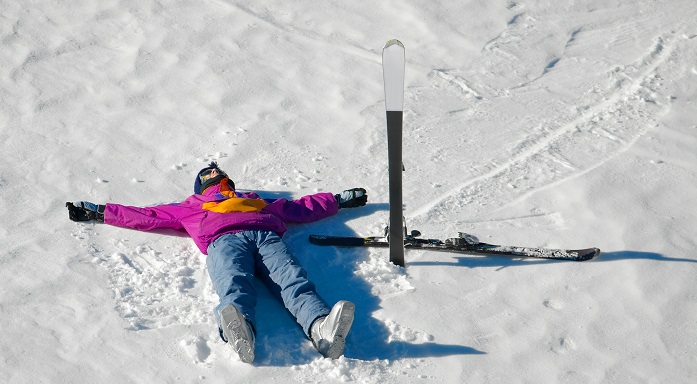 Esquiador vestido de rosa tumbado en la nieve con sus esquís al lado 