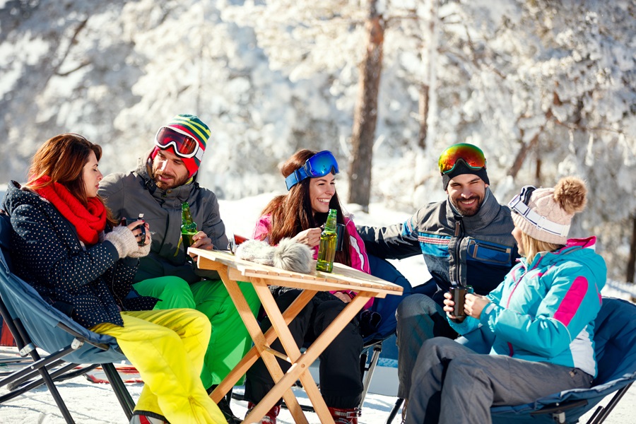 Gente tomando algo en la nieve mientras descansa de un largo día de esquí 