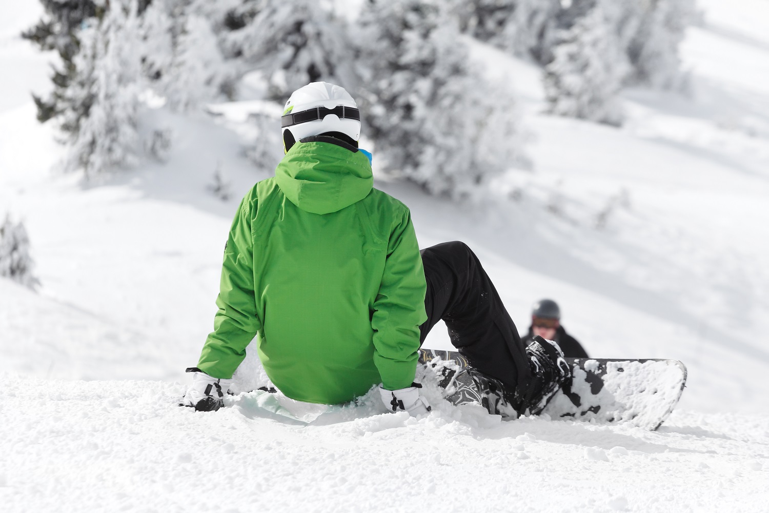 Chico sentado en la nieve con tabla de snowboard en los pies 