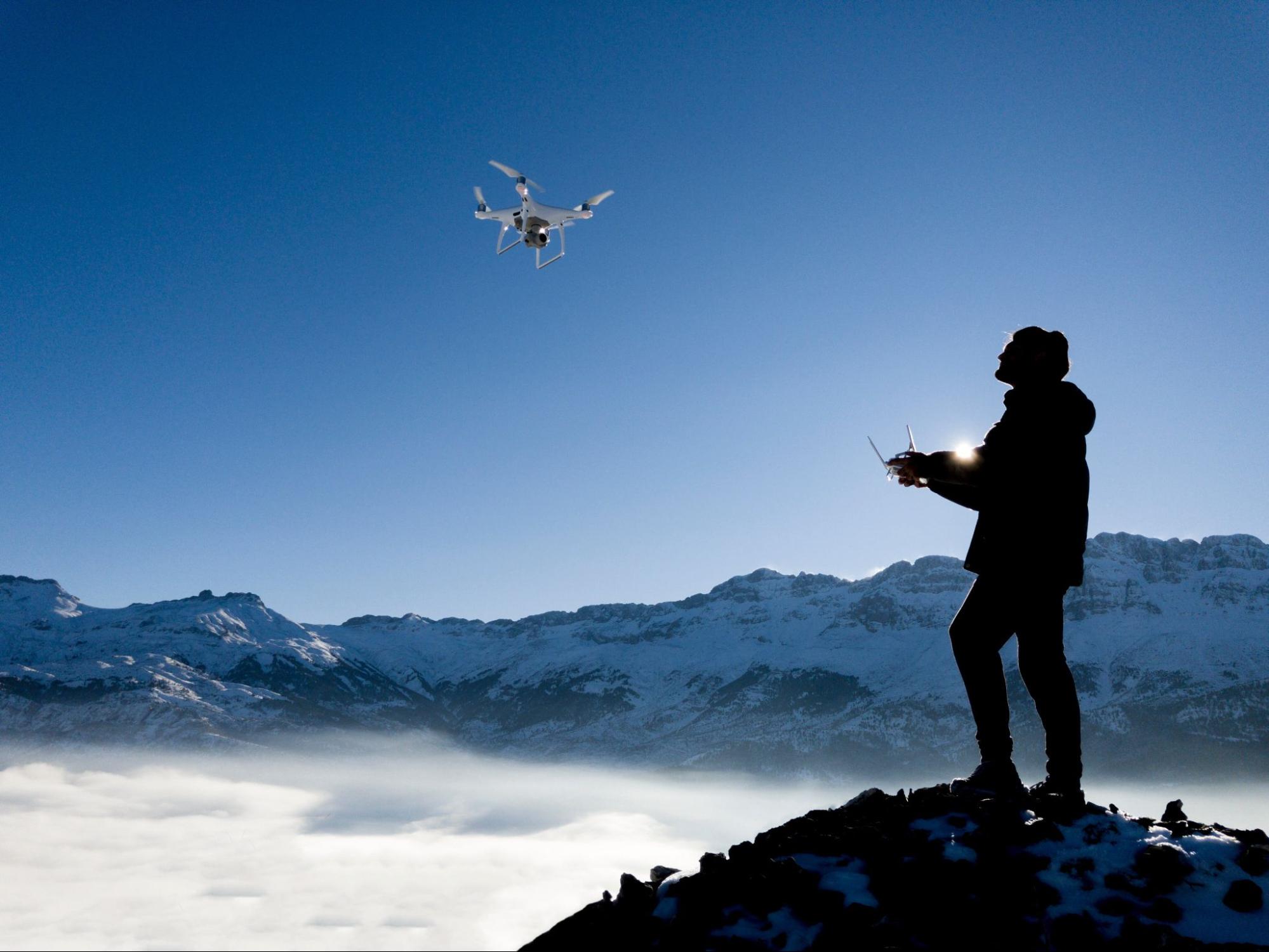 Un hombre pilotando un dron en la cima de una montaña nevada 