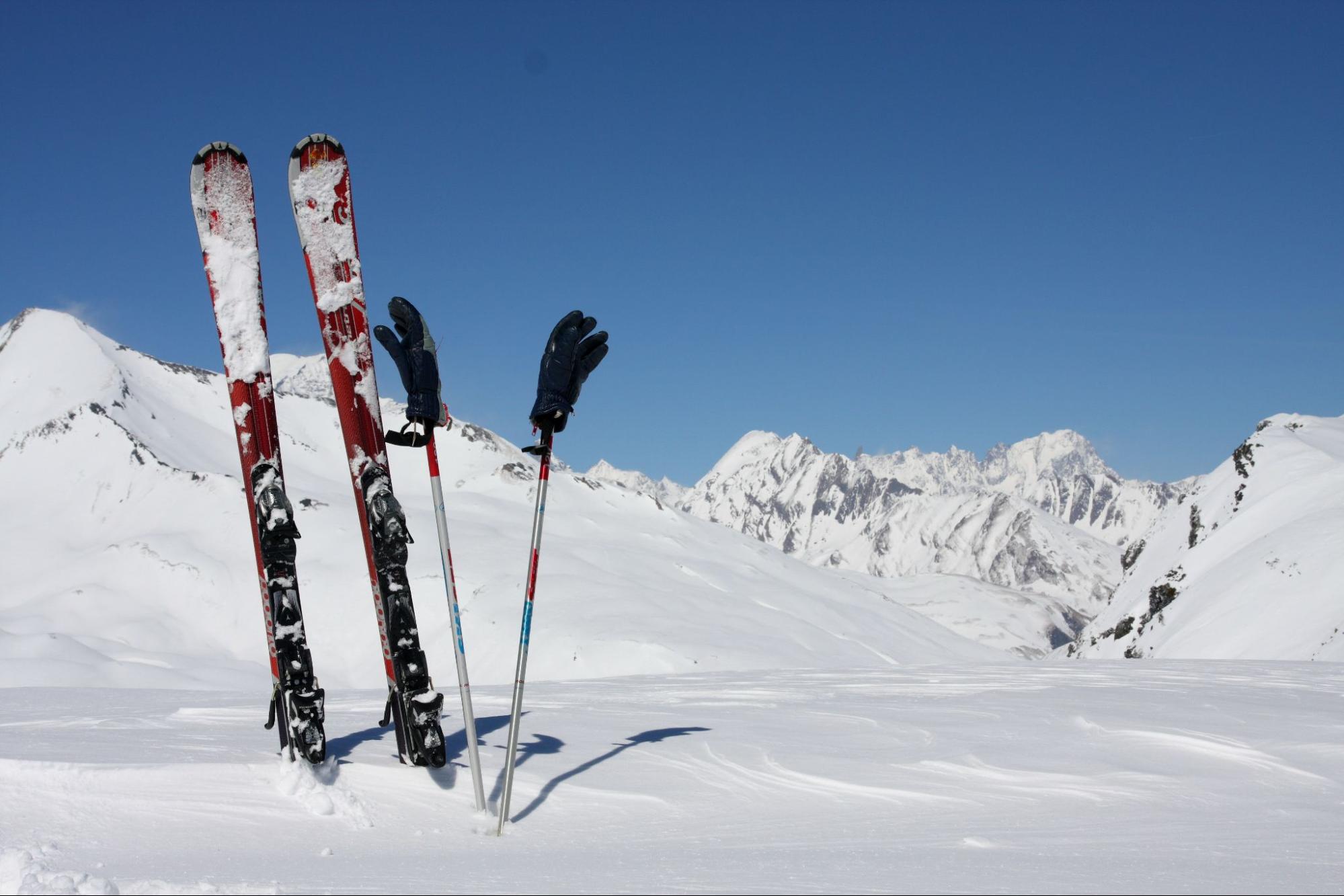 Un par de esquís clavados en la nieve con las montañas nevadas de fondo 